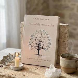 Könnte beinhalten: Ein beiges Journal mit dem Titel "Journal de reconnexion" mit einer Baumillustration. Der Text "RITUEL D'ANCRAGE" steht über dem Titel, und ein Zitat steht unter der Illustration. Eine brennende Kerze, eine Tasse und Kristalle sind ebenfalls im Bild.