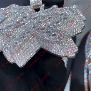 May include: Close-up of a silver pendant and ring set with numerous small, sparkling crystals. The pendant has a unique, layered design. The ring features a large, square-cut crystal. The jewelry is set against a dark background.