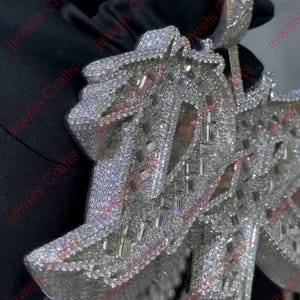 May include: A dazzling, silver-toned pendant necklace, encrusted with numerous small, sparkling stones. The pendant features an intricate, geometric design with a large bail for a chain. The jewelry is displayed against a dark background.