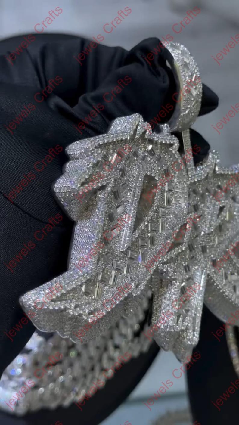 May include: A dazzling, silver-toned pendant necklace, encrusted with numerous small, sparkling stones. The pendant features an intricate, geometric design with a large bail for a chain. The jewelry is displayed against a dark background.