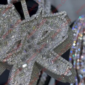 May include: Close-up of a diamond-encrusted pendant. The pendant is shaped like a stylized letter and is covered in small, sparkling diamonds. The background is blurred, highlighting the jewelry.