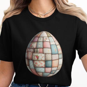 Puede incluir: Camiseta negra con un gran diseño de huevo de Pascua. El huevo está compuesto por parches de tela en colores pastel, incluyendo rosa, azul y verde, con patrones florales y un aspecto de patchwork. El diseño es detallado.