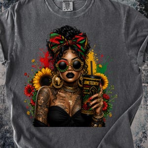 May include: A charcoal gray t-shirt featuring a graphic of a person with dark curly hair, a red, green, and black headwrap, and round sunglasses. The person holds a cup labeled JUNETEENTH CELEBRATE FREEDOM HONOR HERITAGE, surrounded by sunflowers.