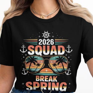 Może przedstawiać: Czarna koszulka z kolorowym nadrukiem graficznym. Projekt zawiera napis "2026 SQUAD BREAK SPRING" z okularami przeciwsłonecznymi odbijającymi scenę plażową, kotwice i koło sterowe.