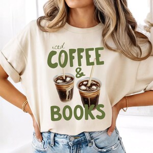 Op de afbeelding: Crèmekleurig T-shirt met de groene tekst "iced COFFEE & BOOKS". Het ontwerp bevat twee ijskoffiedranken met rietjes. Het shirt is een casual, comfortabele stijl.