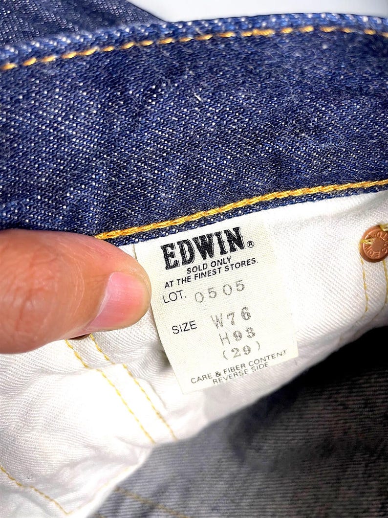 K&ouml;nnte beinhalten: Nahaufnahme der Innenseite einer blauen Jeans. Ein wei&szlig;es Etikett zeigt die Marke "EDWIN" und Gr&ouml;&szlig;enangaben: W76, H93 (29). Das Etikett enth&auml;lt auch den Text "SOLD ONLY AT THE FINEST STORES."