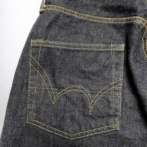 K&ouml;nnte beinhalten: Nahaufnahme einer dunklen Jeans mit einer Ges&auml;&szlig;tasche. Die Tasche ist mit gelben N&auml;hten umrandet, und die Jeans hat ein klassisches F&uuml;nf-Taschen-Design. Der Denim ist dunkel gewaschen.