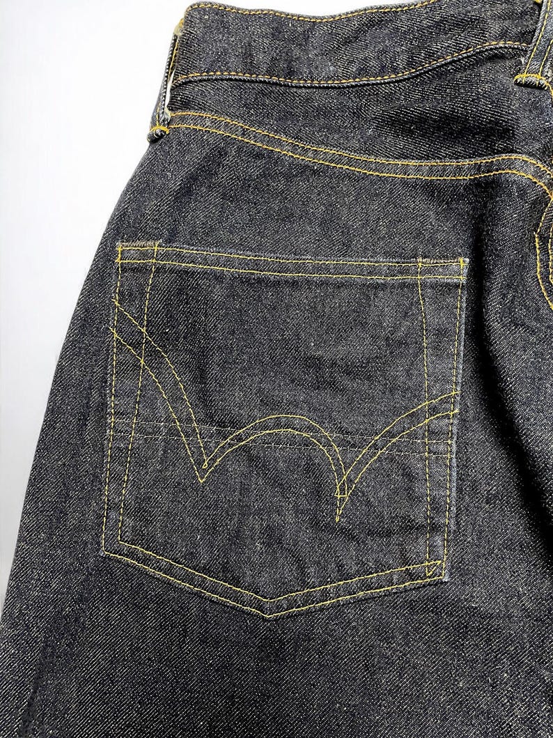 K&ouml;nnte beinhalten: Nahaufnahme einer dunklen Jeans mit einer Ges&auml;&szlig;tasche. Die Tasche ist mit gelben N&auml;hten umrandet, und die Jeans hat ein klassisches F&uuml;nf-Taschen-Design. Der Denim ist dunkel gewaschen.