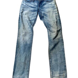 May include: Pale blue denim jeans with a faded wash and subtle distressing. The jeans have a classic five-pocket design, a button and zip closure, and a slim fit. The denim has a worn appearance.