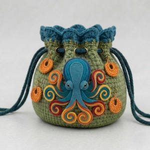 May include: A handmade green crochet drawstring bag featuring a felt octopus design in shades of blue, orange, and yellow. The bag has a teal blue crocheted top and drawstring, with orange crochet accents. The bag is approximately 6 inches in height.