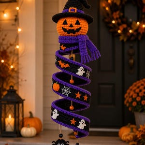 May include: A hanging crochet Halloween decoration featuring an orange jack-o'-lantern head wearing a black witch hat and a purple scarf. A long, spiraling black and purple ribbon is adorned with small white ghosts, orange bats, orange stars, and white spiderwebs.