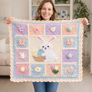 Pode incluir: Um cobertor de crochê em tons pastel com um coelho segurando ovos de Páscoa. O cobertor tem um padrão quadrado com enfeites florais e de ovo. A borda é ondulada e a paleta de cores inclui rosa, azul e amarelo.