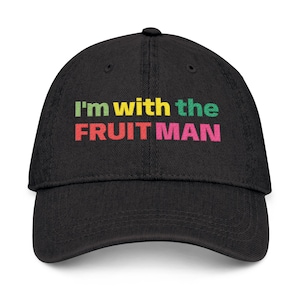 Puede incluir: Gorra de béisbol negra con el texto "I'm with the FRUIT MAN" en amarillo, verde, rojo y rosa. La gorra tiene una visera curva y un botón en la parte superior. Un accesorio casual.