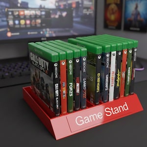 May include: A red game stand holding multiple Xbox One game cases. The cases have green tops and various game titles visible, including "Call of Duty: Black Ops III" and "Forza Horizon 5". The stand has the words "Game Stand" printed on the front.