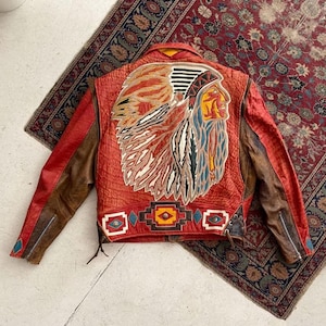 May include: Red leather jacket with a Native American chief design on the back. The jacket has brown sleeves and geometric patterns. A vintage style jacket.