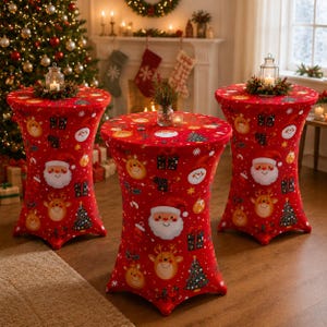 May include: Three tall, cylindrical cocktail tables covered in red spandex fabric featuring a repeating Christmas pattern of Santa Claus faces, reindeer, gift boxes, and pine trees. Each table is topped with a glass lantern and greenery.