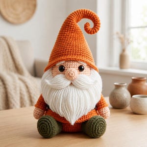 May include: A handmade crochet gnome doll with an orange hat and matching orange shirt. The gnome has a long white beard, a tan face, and green pants. The hat curls at the top. The doll is sitting on a wooden table.