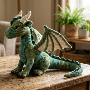 Puede incluir: Un dragón hecho a mano a ganchillo en tonos verdes y azules, con cuernos y detalles de alas color crema. El dragón está sentado sobre una mesa de madera, mostrando sus escamas y alas detalladas. La cola del dragón es larga y tiene una serie de púas.