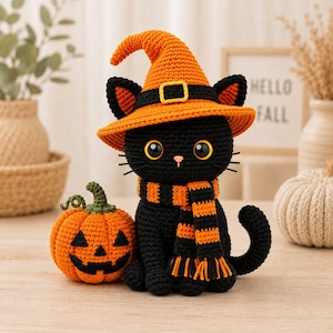 Puede incluir: Una figura de gato tejida a ganchillo de color negro que lleva un sombrero de bruja naranja con una banda negra y una hebilla amarilla, y una bufanda a rayas naranjas y negras. Junto al gato hay una pequeña calabaza tejida de color naranja.