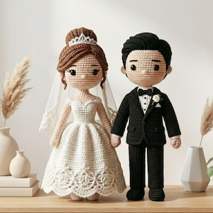 May include: Crocheted bride and groom dolls. The bride wears a white dress, veil, and tiara. The groom is in a black suit with a bow tie and boutonniere. They are holding hands, standing on a wooden surface.