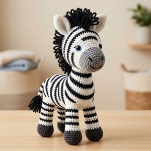 Può includere: Un peluche a forma di zebra realizzato all'uncinetto con corpo bianco a strisce nere, criniera nera e muso grigio. Il giocattolo ha occhi blu e zoccoli grigio scuro. La zebra è in posizione di profilo, evidenziando la trama del filato.