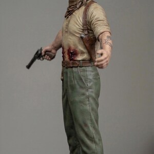 May include: A detailed figurine of a person with short dark hair, wearing a tan long-sleeve shirt with a visible chest wound, a brown neckerchief, a brown leather shoulder holster, green trousers, and brown boots, holding a black revolver in one hand.