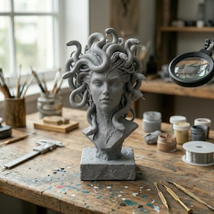 Puede incluir: Un busto escult&oacute;rico gris de una figura con serpientes por cabello, montado sobre una base rectangular. La escultura presenta rasgos faciales detallados y texturas de serpiente intrincadas, situada sobre un banco de trabajo de madera.
