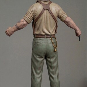 May include: A miniature figurine of a person seen from the back, wearing a tan short-sleeved shirt, olive green trousers, and brown boots. The figure features a brown leather shoulder holster, a gold-coloured pocket watch chain, and a tattoo on the right arm.