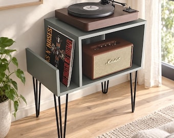 May include: A gray wooden record player stand with black metal hairpin legs. The top surface holds a dark wood turntable. The side compartment stores a Guns N' Roses Appetite for Destruction vinyl record, and the shelf houses a brown Marshall speaker.