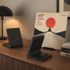 Può includere: Due supporti a forma di L di colore nero opaco progettati per mantenere gli oggetti in posizione verticale. Ogni supporto presenta una base piatta con un piccolo bordo anteriore per fissare gli oggetti. Sono realizzati in materiale solido e liscio.