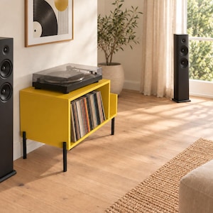 May include: A bright yellow record storage console with a rectangular frame and four thin black legs. The top surface holds a black turntable with a clear dust cover, while the interior compartment contains a collection of vinyl records.
