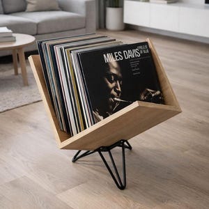 Puede incluir: Un soporte de discos de vinilo de madera con una base de metal negro. El soporte está lleno de discos de vinilo, con el álbum "Kind of Blue" de Miles Davis visible. El soporte está inclinado, mostrando las portadas.
