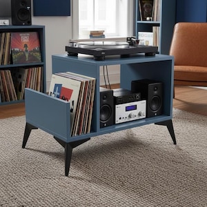 Op de afbeelding: Een blauwe houten mediaconsole met zwarte schuine poten, voorzien van een bovenzijde met een zwarte platenspeler, een zijvak voor vinylplaten en een open plank met een zwarte versterker, een zilverkleurige receiver en twee zwarte luidsprekers.