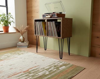 May include: A wooden record player console with two open storage compartments filled with vinyl records, supported by four black metal hairpin legs. A portable record player with a clear lid sits on the top surface of the console.