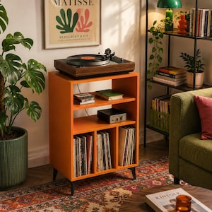 Op de afbeelding: Een feloranje houten platenspelerkast met vier zwarte metalen poten. Het meubel heeft een open bovenblad met een platenspeler, een middelste plank met een elektronisch apparaat en drie verticale onderste vakken gevuld met vinylplaten.