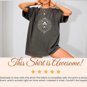 Pu&ograve; includere: T-shirt grigio scuro con un disegno di lupo bianco in una cornice circolare. La maglietta ha maniche corte e una vestibilit&agrave; ampia. Il testo "This Shirt is Awesome!" &egrave; visualizzato sotto.
