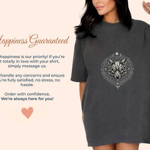 Pu&ograve; includere: T-shirt grigio scuro con un design dettagliato di testa di lupo all'interno di un cerchio geometrico. La maglietta ha maniche corte e una vestibilit&agrave; ampia. Il testo "Happiness Guaranteed" &egrave; visualizzato in un carattere decorativo.