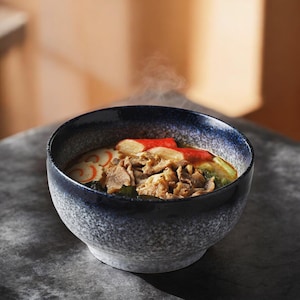 May include: A bowl of Japanese ramen with visible steam. The bowl has a speckled blue and gray design. The ramen includes crab sticks, meat, and other ingredients.