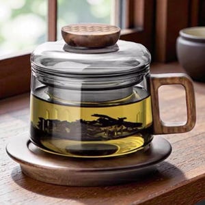 May include: A clear glass tea infuser mug with a wooden handle, lid, and coaster. The mug contains brewed tea. The wooden lid has a textured design. The mug sits on a wooden coaster, and the background is a wooden surface.