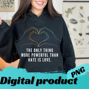 Può includere: Felpa con cappuccio nera con un design a forma di cuore con le mani in arancione e verde acqua. Il testo recita: "THE ONLY THING MORE POWERFUL THAN HATE IS LOVE." Sono visibili anche le parole "Prodotto digitale" e "PNG".