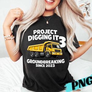 May include: Black t-shirt with the text "PROJECT DIGGING IT 3" and a yellow dump truck graphic. The shirt also includes the text "GROUNDBREAKING SINCE 2023".