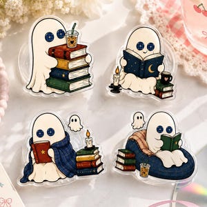 May include: Four acrylic charms featuring white ghost characters with blue button eyes. Each ghost is depicted in various reading scenes with stacks of colorful books, candles, blankets, and iced coffee drinks. The designs are clear, flat, and illustrated.