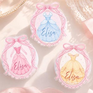 May include: Three oval-shaped stickers featuring watercolor illustrations of princess gowns in blue, pink, and yellow. Each sticker has a pink ribbon and the name "Elisa" in cursive.
