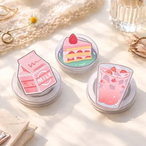 May include: Three clear acrylic coasters with food illustrations. One coaster features a pink strawberry milk carton with the word "MILK". Another shows a slice of strawberry cake. The third depicts a pink strawberry drink.