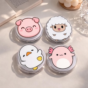 May include: Four clear, round containers with cartoon animal designs. The designs include a pink pig, a white sheep, a white chick, and a pink axolotl. Each container has a clear lid and a gray rim. The containers are arranged on a light-colored surface.