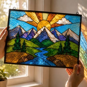 May include: Stained glass panel depicting a mountain landscape with a vibrant sunset. The artwork features a blue sky with white clouds, snow-capped mountains, green hills, and a blue river. The sun radiates orange and yellow hues.