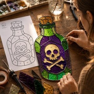 Artisan assembling a Halloween poison bottle stained glass suncatcher on a wooden workbench using a numbered printable pattern, colorful glass pieces, and stained glass tools. Beginner-friendly digital download includes SVG, PNG, JPG, and PDF files with a commercial license, perfect for DIY stained glass projects, Halloween décor, gothic crafts, witchy home decorations, and handmade gifts.