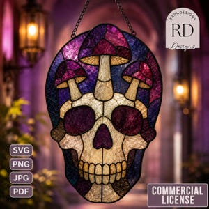 May include: A stained glass suncatcher featuring a skull design with three mushrooms growing from the top. The piece uses textured glass in shades of purple, blue, and cream, held together by black metal cames. A hanging chain is attached to the top.