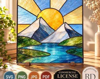 May include: A square stained glass panel featuring a landscape with a bright yellow sun, blue sky, white and dark blue mountain peaks, and a blue river flowing through green hills. The panel is framed in black metal and stands on two small wooden blocks.