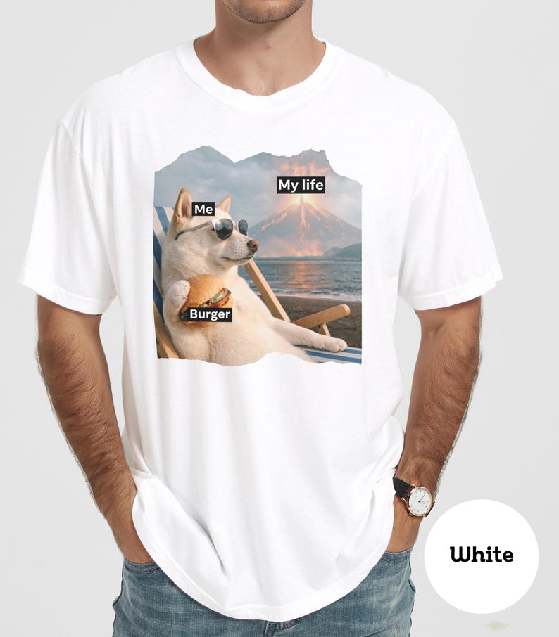 May include: White t-shirt featuring a dog wearing sunglasses, holding a burger, and relaxing in a beach chair. The shirt has the text "Me", "Burger", and "My life" in black boxes, with a volcano and ocean background.